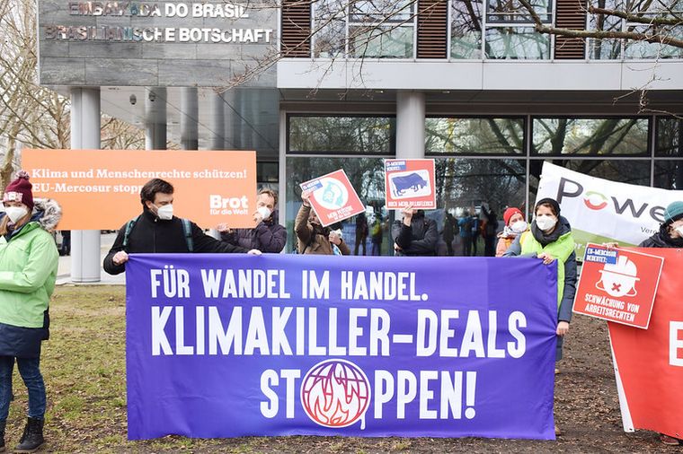 Vertreter*innen verschiedener NGOs bei der Protestkundgebung. Auf dem Transparent im Vordergrund steht "Für Wandel im Handel. Klimakiller-Deals stoppen!"