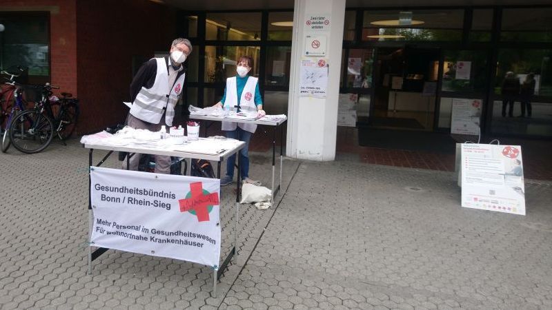 Zwei Menschen stehen hinter einem Sammeltisch für das Krankenhausvolksbegehren NRW