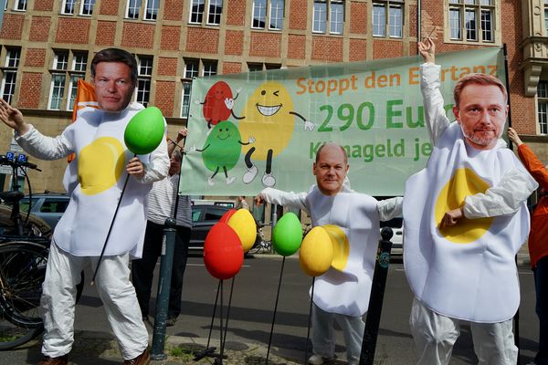Vor der Parteizentrale der FDP stehen drei Menschen in Spiegeleikostümen mit Masken von Habeck, Lindner und Scholz, die mit bunten Eiern spielen, hinter ihnen ist ein Transparent mit der Aufschrift "Stoppt den Eiertanz: 290€ Klimageld jetzt!"