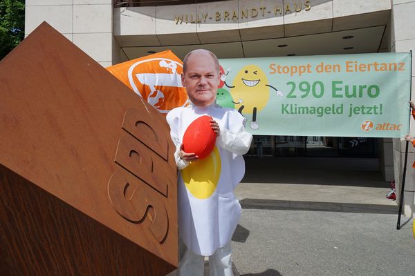 Das Ei mit Olaf-Scholz-Maske steht neben dem SPD-Würfel vor dem Willy-Brandt-Haus, im Hintergrund ist das Banner mit dem Text "Stoppt den Eiertanz: 290€ Klimageld jetzt!"