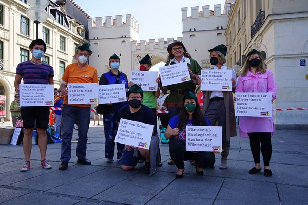 Gruppenbild des Bündnisses vorm Karlstor, die neun Teilnehmer*innen halten Schilder mit Umverteilungsforderungen in der Hand.