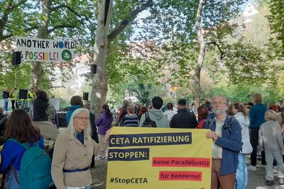 Zwei Menschen stehen auf einer Demo und halten ein Schild mit der Aufschrift "CETA-Ratifizierung stoppen – keine Paralleljustiz für Konzerne"