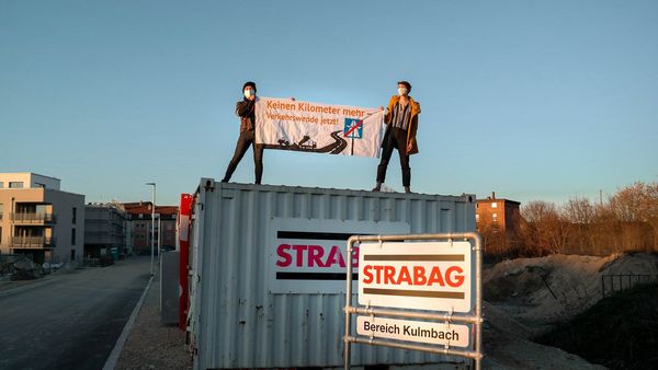 Zwei Aktivist:innen stehen auf einem Strabag-Container und halten ein Transparent mit der Aufschrift "Keinen Kilometer mehr – Verkehrswende jetzt!"