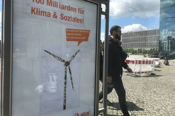 Vor dem Berliner Hauptbahnhof hängt ein geadbustetes Werbeplakat auf dem ein Windrad in Camouflage mit einer Sprechblase auf der "Muss ich Tarnflecke tragen, damit es Geld für das Klima gibt?" steht. Als Überschrift steht "100 Milliarden für Klima und Soziales!" auf dem Plakat