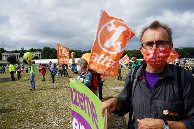 Auf der Auftaktkundgebung der IAA-Demo 2021 schaut ein Aktivist mit Gesichtsmaske freundlich in die Kamera, daneben weht eine Attac-Fahne