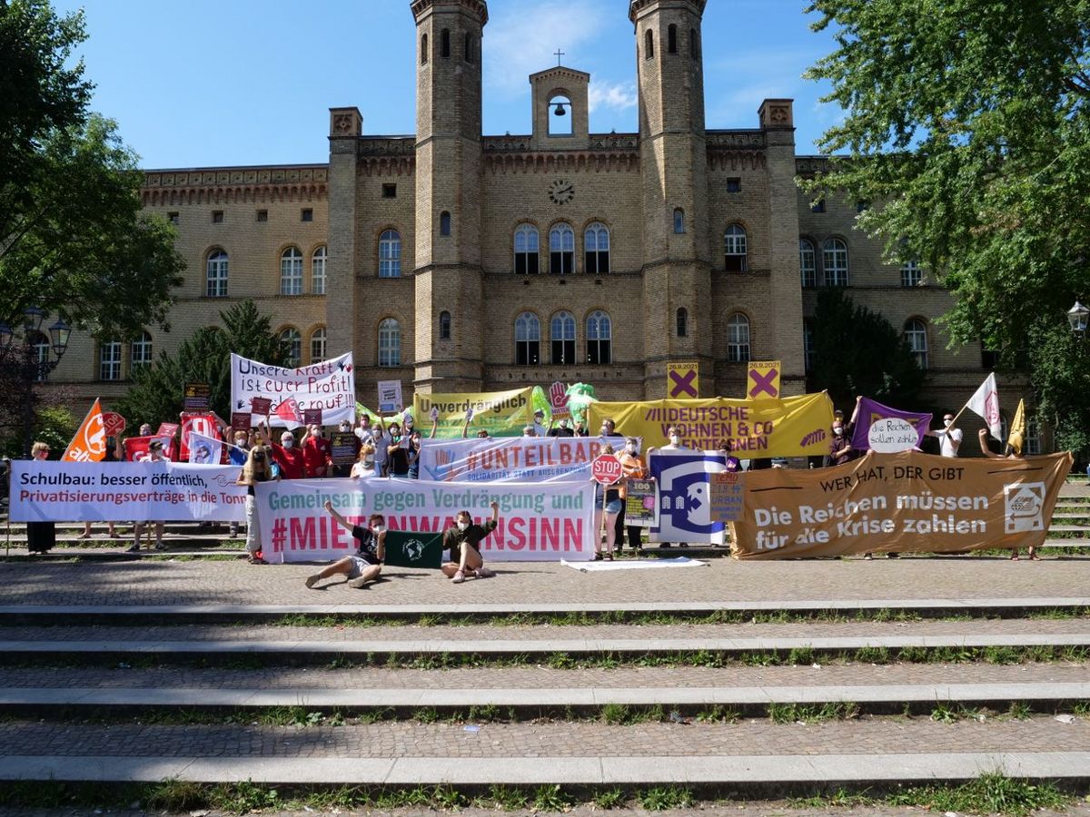 Vor dem Betanken in Berlin-Kreuzberg stehen Aktivist*innen mit vielen verschiedenen Bannern und Fahnen, von Attac, über Deutsche Wohnen und Co. Enteignen bis zu #Unteilbar