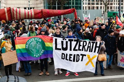 Demonstrant*innen halten eine FFF-Regenbogenfahne und ein Transparent mit dem Slogan "Lützelrath bleibt"