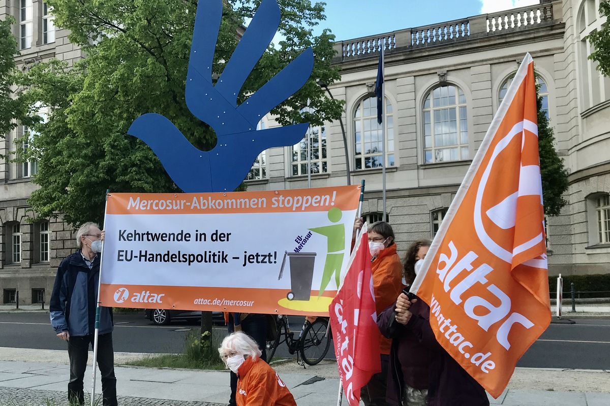 Attachés halten ein Banner mit dem Slogan "Kehrtwende in der EU-Handelspolitik – jetzt!", im Hintergrund ist ein übergroßes Menschenrechtssymbol aus Holz