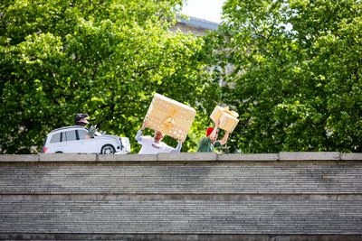 Zwei Aktivist*innen tragen in Gold verpackte Geschenke und laufen vor dem als Auto mit Saurierkopf verkleideten Aktivisten weg.