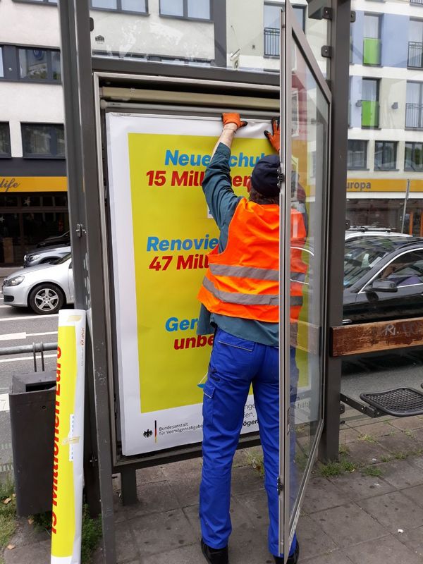 Eine Person in Warnweste hängt Plakate in einen Werbekasten