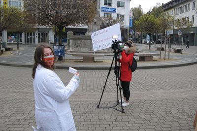 Eine Aktivistin im weißen Kittel hält Akstionsmaterial in die Kamera eines Filmteams.