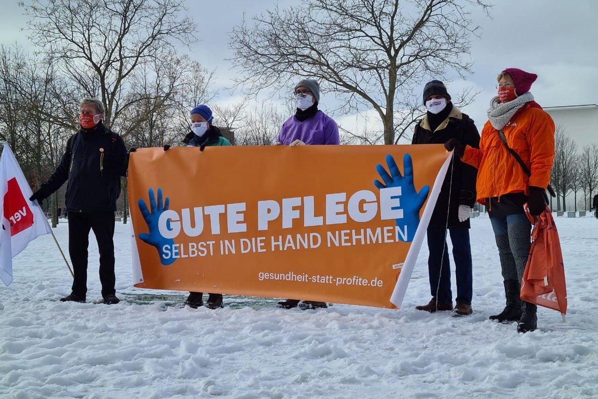 Menschengruppe steht im Schnee mit einem Banner auf dem "Gute Pflege selbst in die Hand nehmen" steht