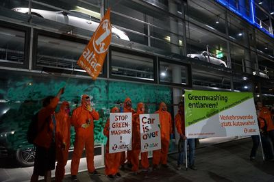Gruppenbild der Aktivist*innen in orangen Overalls vor der angesprühten Scheibe mit Attac-Fahne und einem Transparent mit der Aufschrift "Greenwashing entlarven"