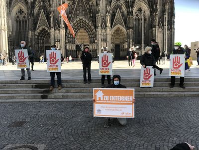 Vor dem Kölner Dom Stehen Aktivist*innen verschiedene Schilder mit mieterpolitischen Forderungen hoch halten.