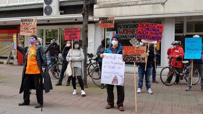 Aktivist*innen stehen mit Protestschildern auf Abstand bei einer Kundgebung