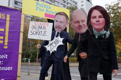 Baerbock und Scholz wählen die Tür mit "Politik für Reiche" aus und Christian Lindner kommt als Zone herausgesprungen. Er hält ein Schild, das Reichenschutz statt Klimaschutz fordert.