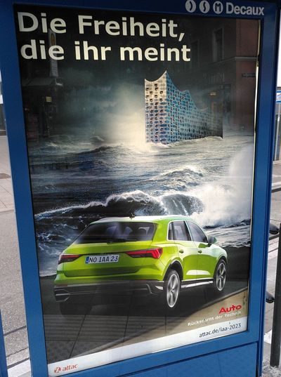 In einem Werbeschaukasten hängt ein gefaktes Plakat, das wie eine Autowerbung aussieht, in der ein dicker SUV vor einem im Meer versunkenen Hamburg fährt, mit dem Slogan "Die Freiheit, die ihr meint"