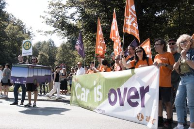 Blick auf den Attac-Block links sieht man einen als Bus verkleideten Aktivisten, rechts das Fronttransparent mit dem Slogan "Car is over" und dahinter mehrere Menschen mit Attac-Fahnen