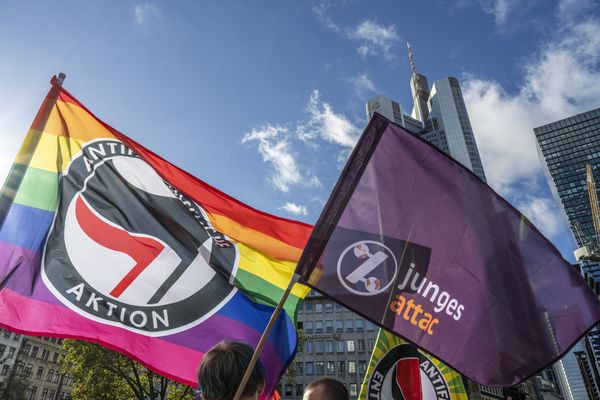 Nebeneinander sind eine junges-Attac- und eine Antifa-Regenbogenfahne vor der Frankfurter Skyline zu sehen