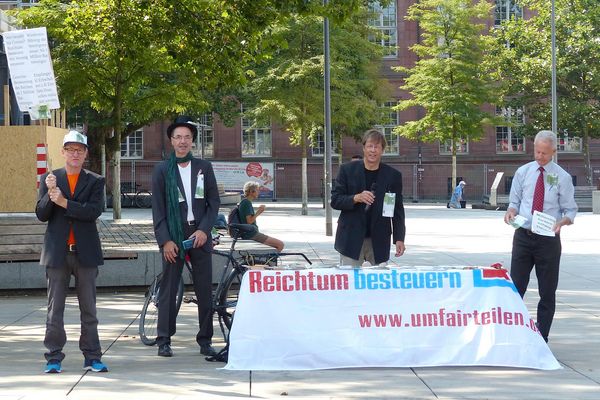 An einem Infostand stehen mehrere Attacis, die Flyer verteilen, die wie 100€ Scheine aussehen
