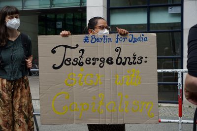 Eine Demonstrantin hält ein Schild mit der Aufschrift "#BerlinforIndia Testergebnis: Sick with Capitalism"