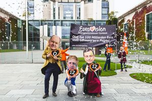 Scholz, Johnson und Draghi hocken vor dem Kanzleramt mit ihren Punkten. Im Hintergrund sieht man das Transparent mit dem Slogan "Eurovision Übersteuergewinn Contest. Olaf, hol 100 Milliarden Euro statt Germany Zero Points"