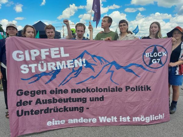Im Bild halten mehrere junge Menschen ein rosa Banner mit der Aufschrift "Gipfel stürmen! Gegen eine neokoloniale Politik der Ausbeutung und Unterdrückung – eine andere Welt ist möglich"
