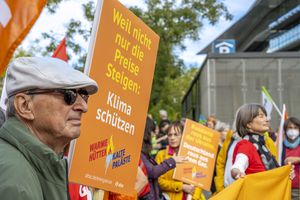 Ein Mann hält ein oranges Schild mit der Aufschrift "Weill nicht nur die Preise steigen: Klima schützen", im Hintergrund ist die Kundgebung zu sehen
