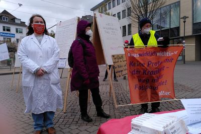 Attacis bei der Kundgebung, im Vordergrund "Profit forte"-Packungen, ein Attac hält ein Handtransparent mit der Aufschrift "#waswirklichwichtigist Keine Profite mit Krankenhäusern in der Pandemie: Fallpauschalen abschaffen"