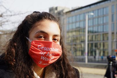 Eine junge Aktivistin hat eine Maske auf, auf der "Gesundheit ist keine Ware" steht