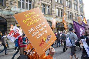 Im Vordergrund ist ein Oranges Schild mit der Aufschrift "Sozial geht nicht national: AfD und Co. sind keine Lösung" zu sehen, im Hintergrund sieht man den Demonstrationsblock