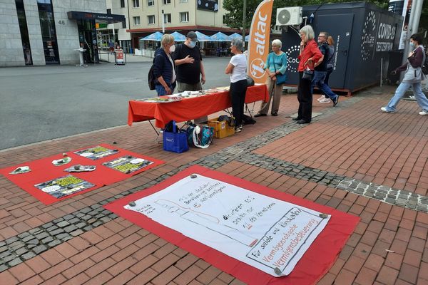 Im Bild ist ein Infostand mit Attacies, im Vordergrund ist ein Plakat, das die Vermögensverteilung in Deutschland mit der Höher der dahinter liegenden Reinholdikirche Vergleicht und erklärt, dass die reichsten 10 Prozent 67 Prozent des Gesamtvermögens besitzen, während die ärmere Hälfte gerade ein Prozent besitzt.