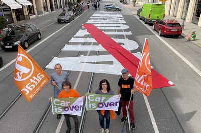 Vor dem Autobahn-Text stehen vier Menschen mit Attac-Fahnen und kleinen Bannern, auf denen "Car is over" steht