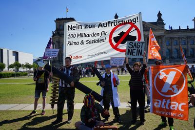 Eine Gruppe Demonstrant*innen steht vor dem Reichstag mit Attac-Fahnen und einem Banner mit der Aufschrift "Nein zur Aufrüstung! 100 Milliarden für Klima und Soziales!"