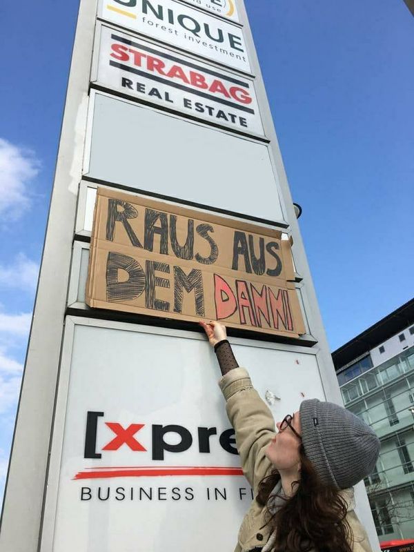 Eine Aktivistin hält ein Schild mit der Aufschrift "Raus aus dem Danni" unter das Firmenschild von Strabag