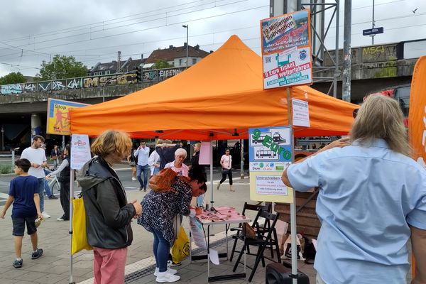 Ein Oranger Pavillon mit einem Infostand, an dem Unterschriften gesammelt werden und Menschen zum Unterschreiben anstehen.