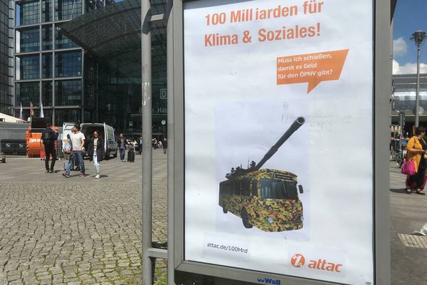 Vor dem Berliner Hauptbahnhof hängt ein geadbustetes Werbeplakat auf dem ein Bus in Tarnfarben mit einem Panzerrohr ist mit einer Sprechblase auf der "Muss ich erst schießen, damit es Geld für den ÖPNV gibt?" steht. Als Überschrift steht "100 Milliarden für Klima und Soziales!" auf dem Plakat