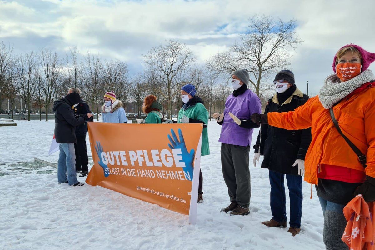 Menschengruppe steht im Schnee mit einem Banner auf dem "Gute Pflege selbst in die Hand nehmen" steht