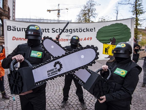 Zwei Als Robocops verkleidete Aktivist*innen  haben Kettensägen mit dem Logo der Grünen auf dem Seegeblatt in der Hand.