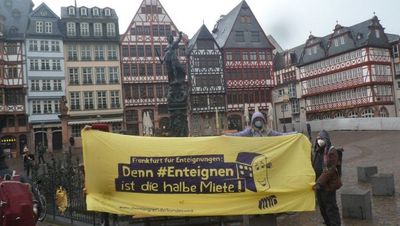 Aktivist*innen halten ein Transparent auf dem Römerberg mit der Aufschrift "Denn #Enteignen ist die halbe Miete!"