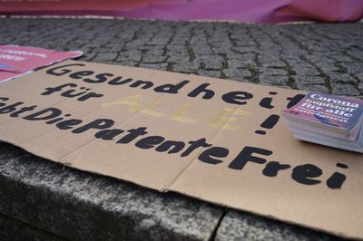 Auf dem Boden liegt ein Pappschild mit der Aufschrift "Gesundheit für alle! Gebt die Patente frei"