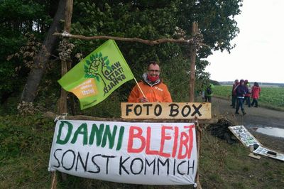 Attac-Aktivist steht in einer Fotobox am Waldrand des Dannenröder Forstes. Unter der Fotobox steht der Slogan "Danni bleibt sonst komm ich"