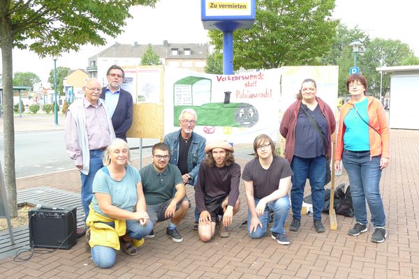 Vor einem Transparent mit dem Slogan "Verkehrswende statt Pofallawende" und einer gemalten Dampflok steht und hockt eine Gruppe von Menschen