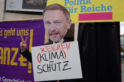 Eine Nahaufnahme von Lindner der vor der Politik für Reiche Tür steht und ein Victory Zeichen macht