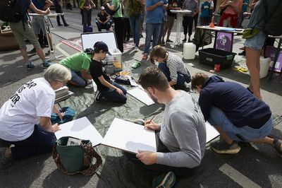 Menschen sitzen auf der Straße im Kreis und malen Demoschilde