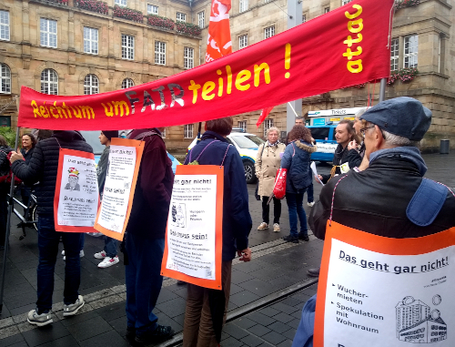 Mehrere Attacies halten auf einer Demo ein Banner mit dem Text "Reichtum umverteilen!"