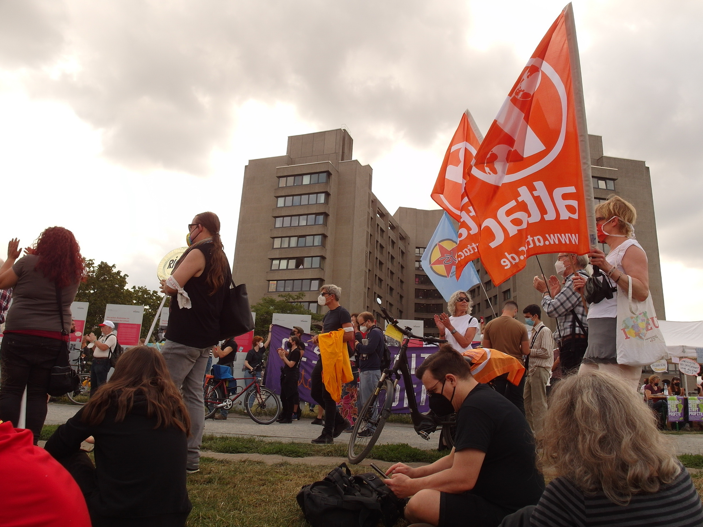 Im Vorderrund die Demo mit Attac-Fahnen, im Hintergrund ist das Urban-Krankenhaus zu sehen
