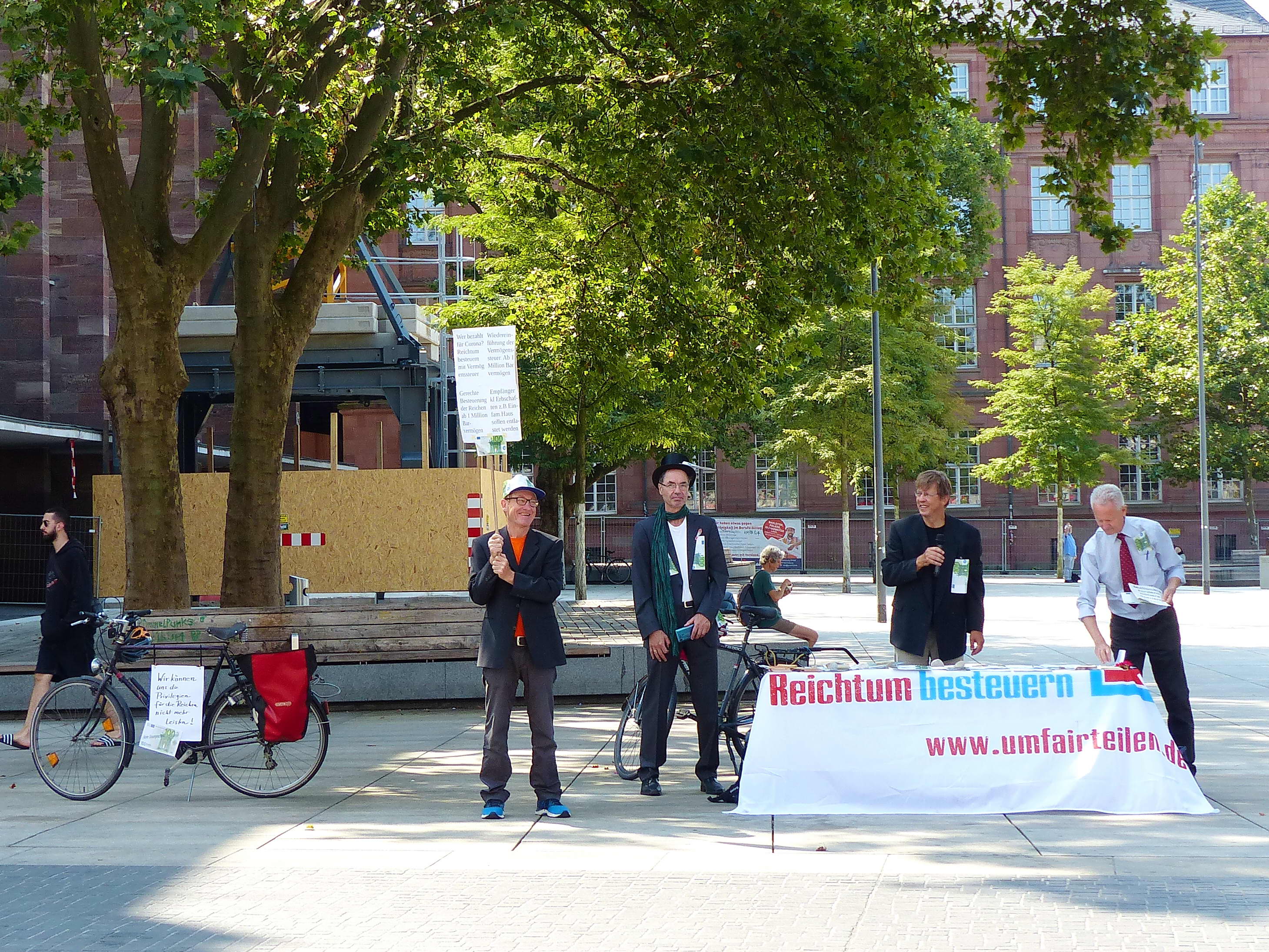 An einem Infostand stehen mehrere Attacis, die Flyer verteilen, die wie 100€ Scheine aussehen