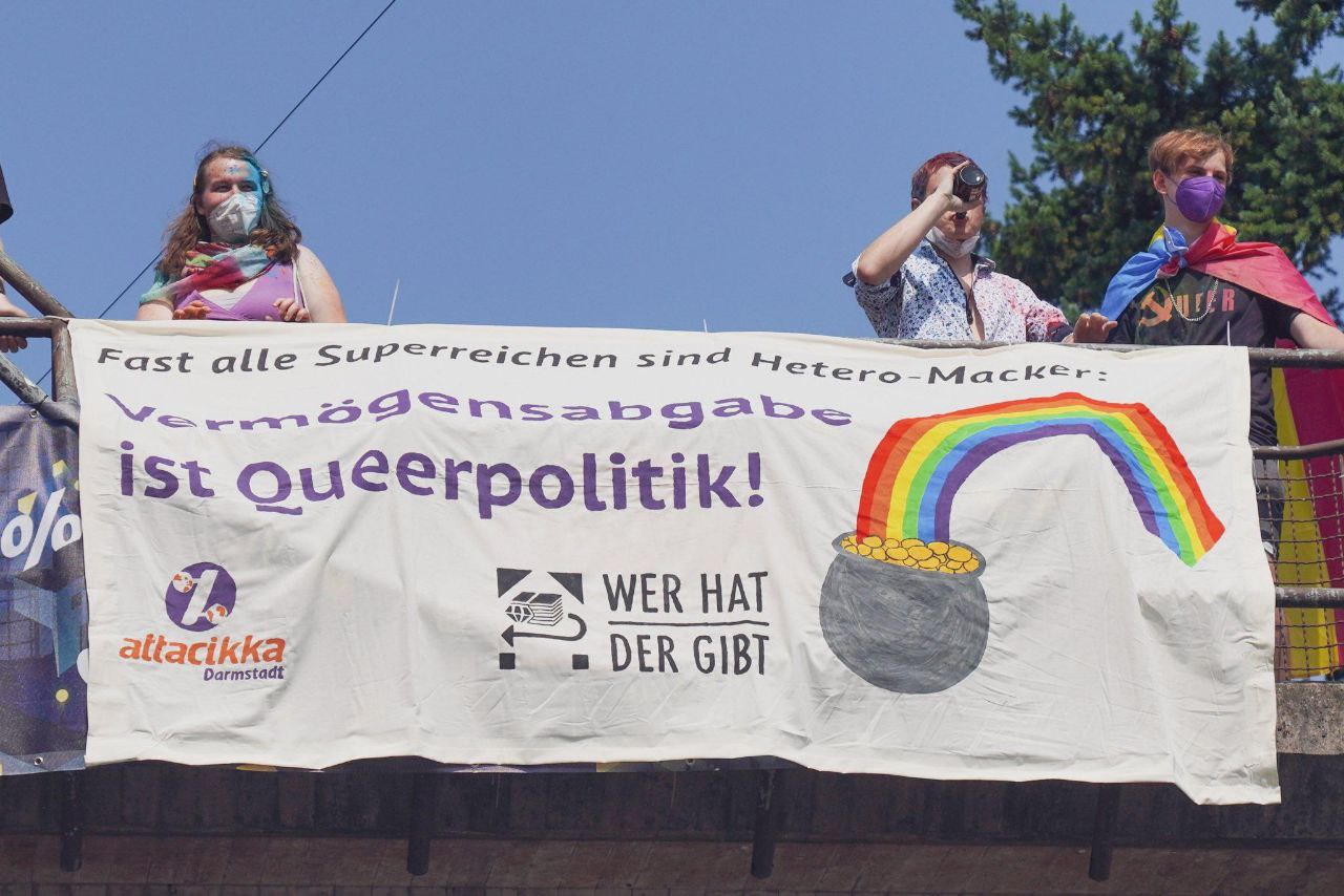 An einer Brücke hängt ein Transparent mit der Aufschrift "Fast alle Superreichen sind Hetero-Macker: Vermögensabgabe ist queerpolitik"