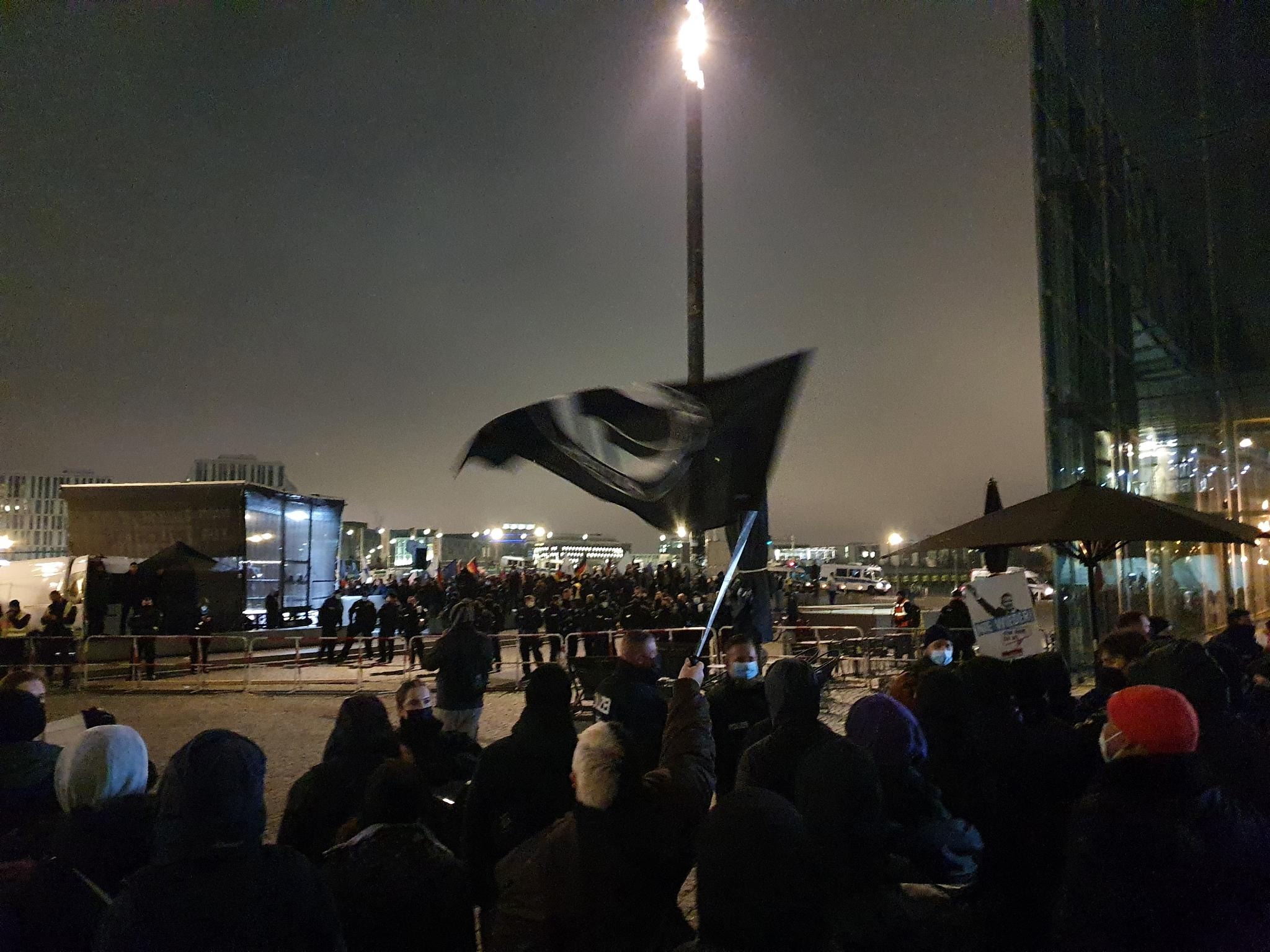 Eine Gruppe von antifaschistischen Demonstrant:innen steht im dunklen der Polizei gegenüber. In der Bildmitte wird eine schwarze Antifafahne geschwenkt.
